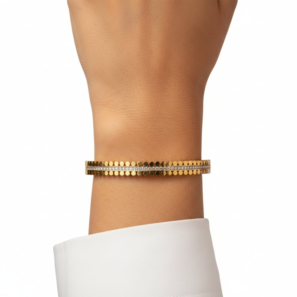 A gold tennis bracelet with a center row of small clear stones, shown worn on a person's wrist against a white background.