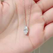 A silver chain necklace with a marquise-cut clear gemstone pendant, held in the palm of a hand.