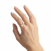 A gold ring with three small white pearls, worn on the ring finger of a hand against a plain white background.