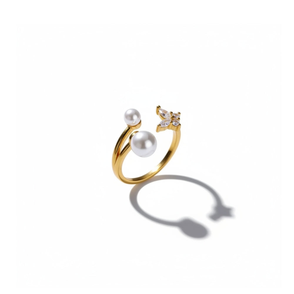 A gold open ring featuring two white pearls and a small butterfly embellishment with clear stones, shown on a clean white background with a soft shadow.