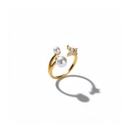 A gold open ring featuring two white pearls and a small butterfly embellishment with clear stones, shown on a clean white background with a soft shadow.