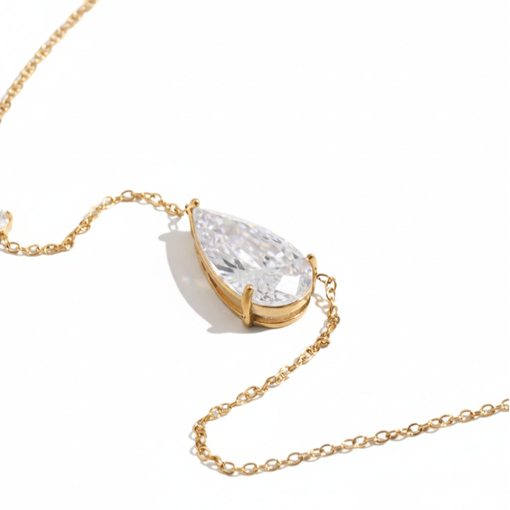 A gold chain necklace featuring a teardrop-shaped clear gemstone pendant in a gold bezel setting, photographed on a clean white background.