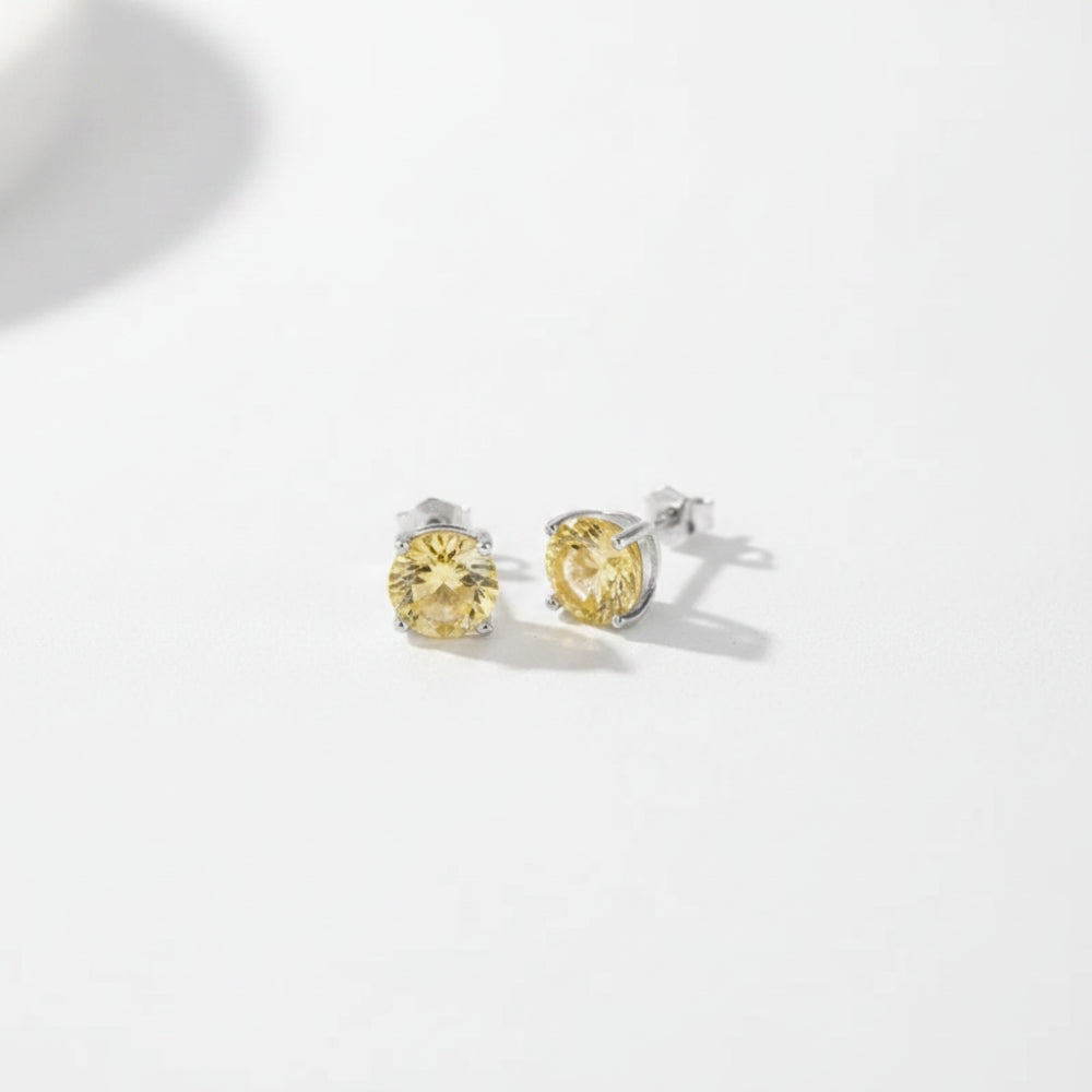 A pair of round yellow gemstone stud earrings in silver settings, photographed on a clean white background with soft shadows.