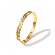 A gold bangle bracelet featuring a textured beaded outer edge and a central channel set with small clear stones, shown on a white background with a soft shadow.
