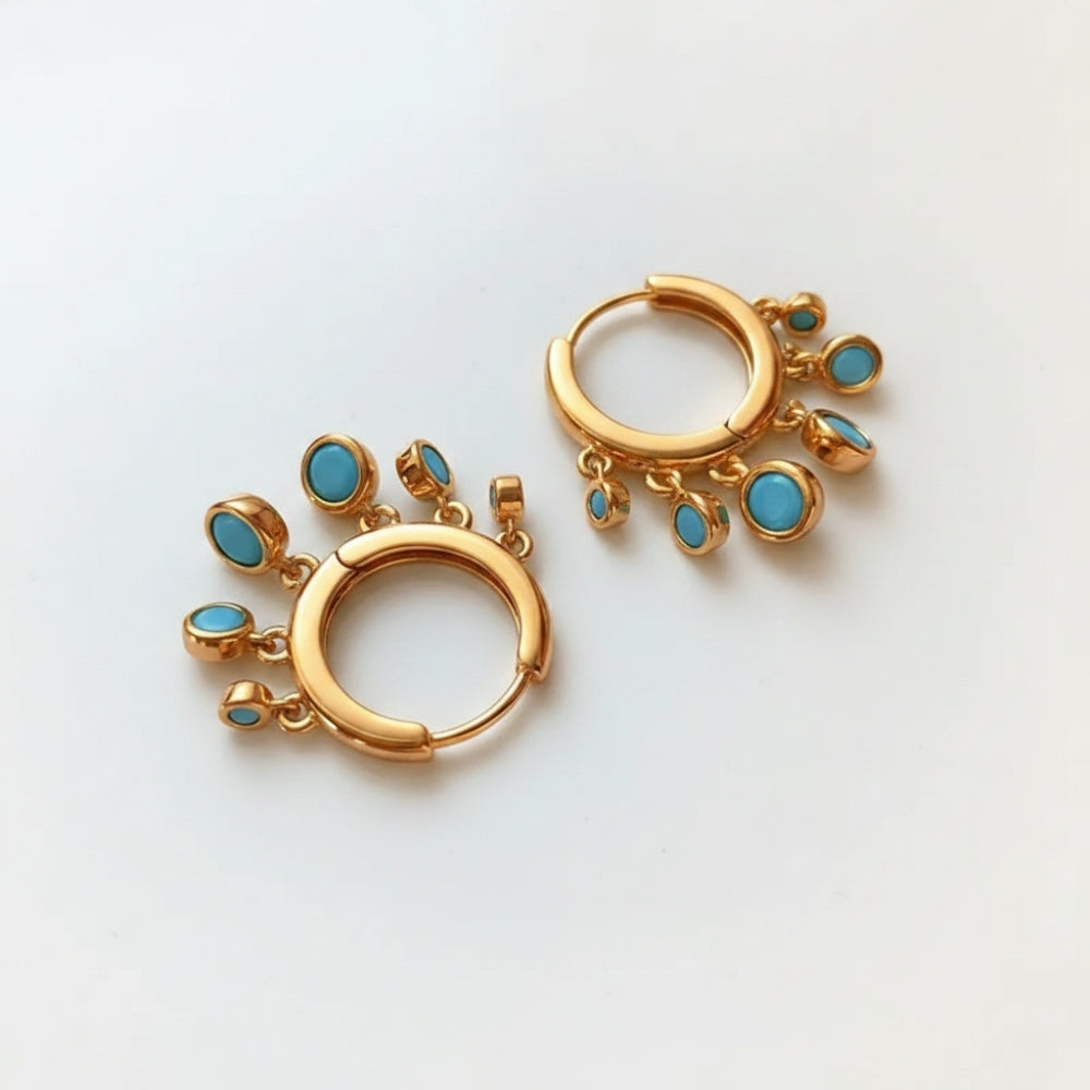 A pair of gold huggie hoop earrings decorated with small dangling turquoise blue stones, displayed on a clean white background.