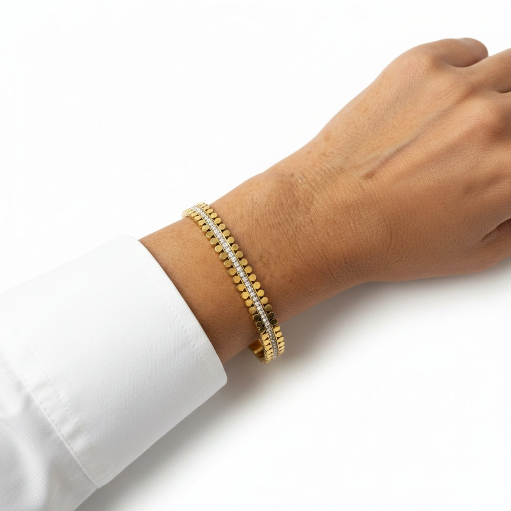 A gold tennis bracelet with a center row of small clear stones, shown worn on a person's wrist against a white background.