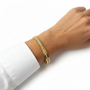 A gold tennis bracelet with a center row of small clear stones, shown worn on a person's wrist against a white background.