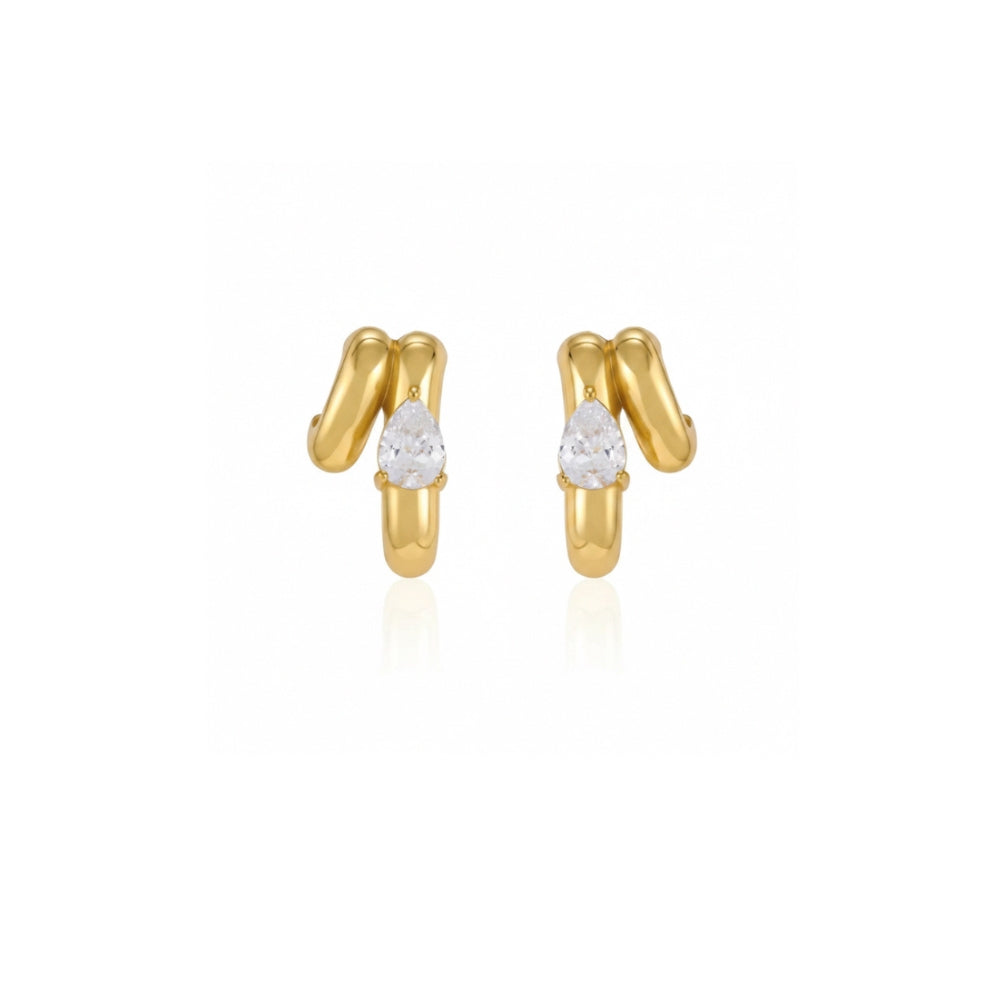 A pair of gold huggie hoop earrings with a small pear-cut clear gemstone in the center of each earring, set against a plain white background with a soft reflection below.