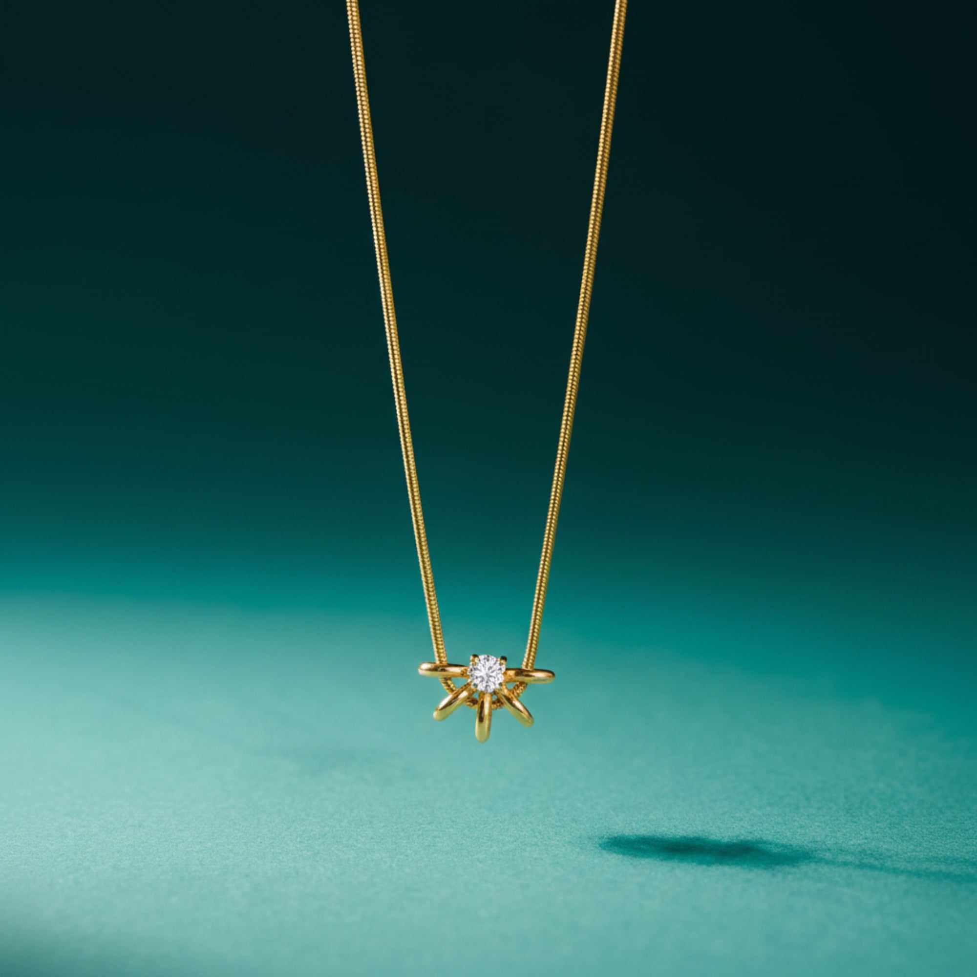 A delicate gold chain necklace with a small gold starburst pendant featuring a central clear gemstone, suspended against a dark teal background.