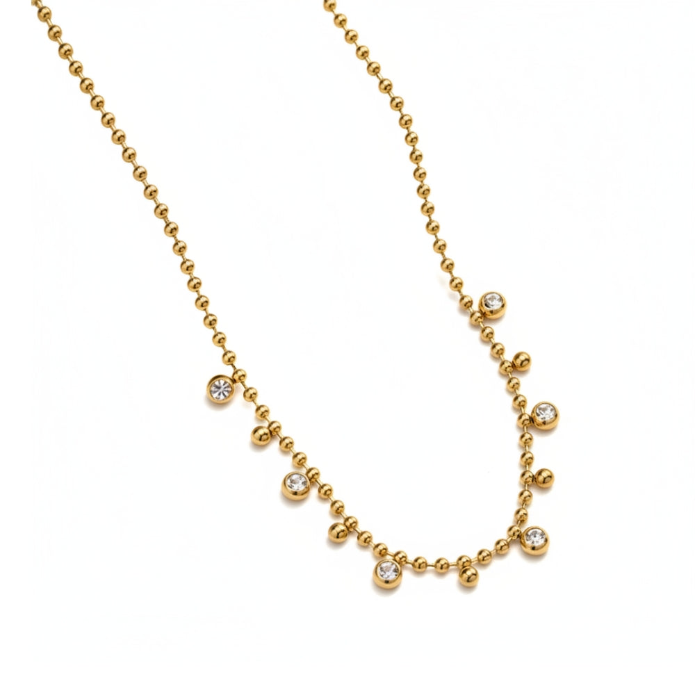 A gold ball-chain necklace featuring six small, bezel-set clear round gemstones spaced along the chain, displayed on a clean white background.