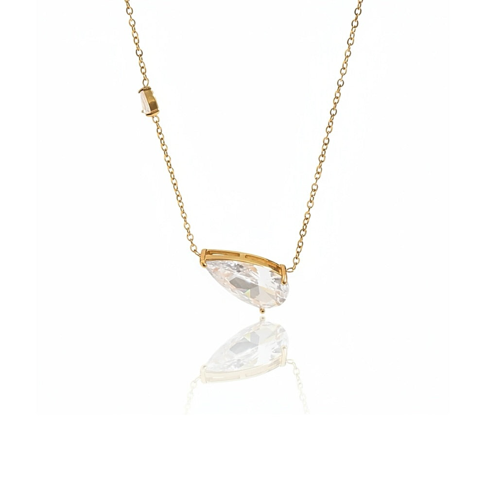 A gold chain necklace with a marquise-cut clear crystal pendant, displayed against a clean white background with a soft reflection below.