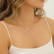 A close-up of a woman wearing a delicate gold necklace with three small white pearls, styled with a white camisole top.