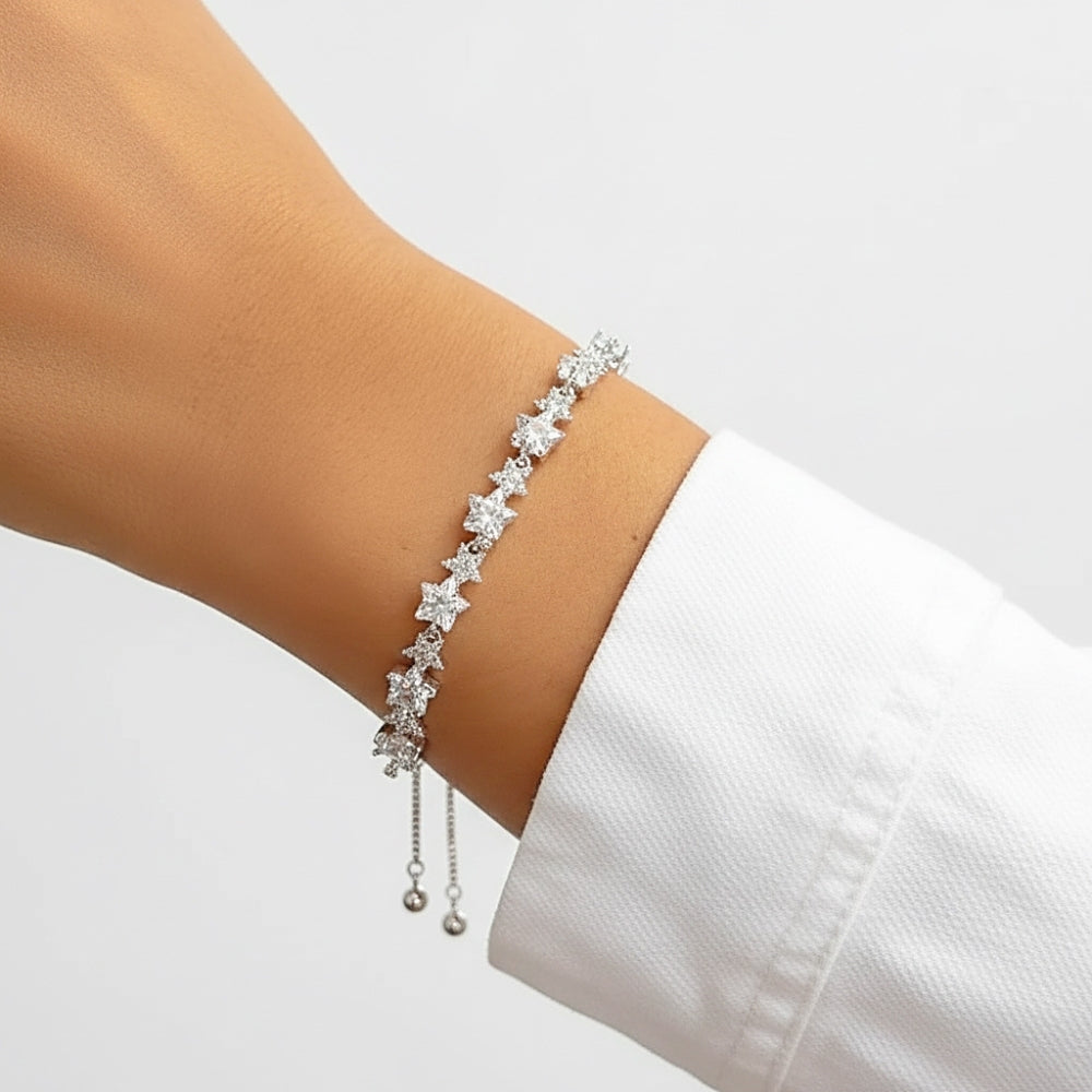 A delicate silver bracelet with star-shaped clear crystals and dangling bead chains, shown worn on a person's wrist with a white shirt cuff visible against a light gray background.