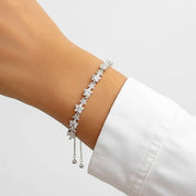 A delicate silver bracelet with star-shaped clear crystals and dangling bead chains, shown worn on a person's wrist with a white shirt cuff visible against a light gray background.