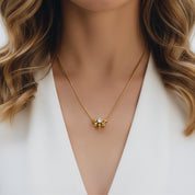 A close-up of a woman wearing a delicate gold necklace with a small gold pendant featuring a clear crystal in the center, styled with a white blazer.