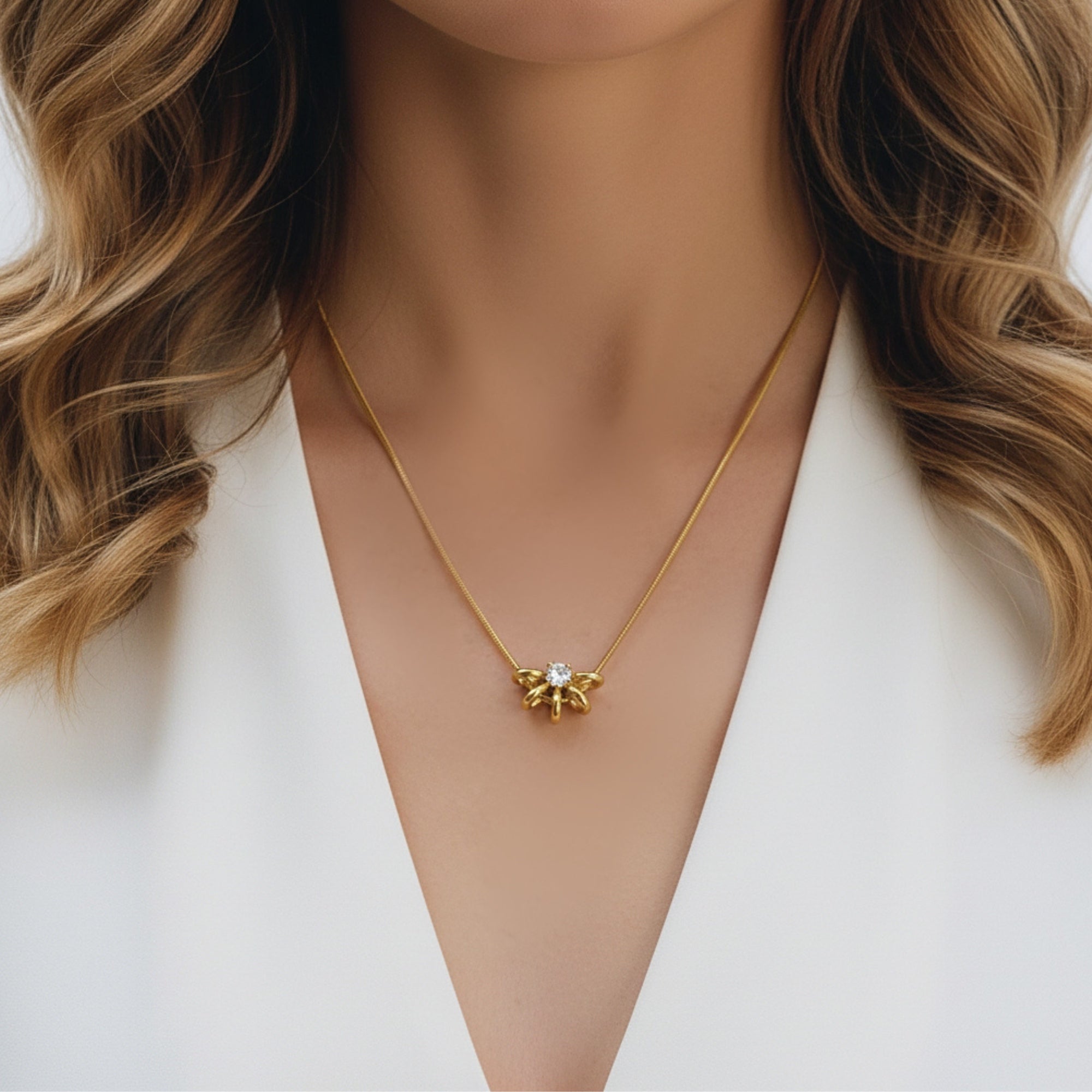 A close-up of a woman wearing a delicate gold necklace with a small gold pendant featuring a clear crystal in the center, styled with a white blazer.