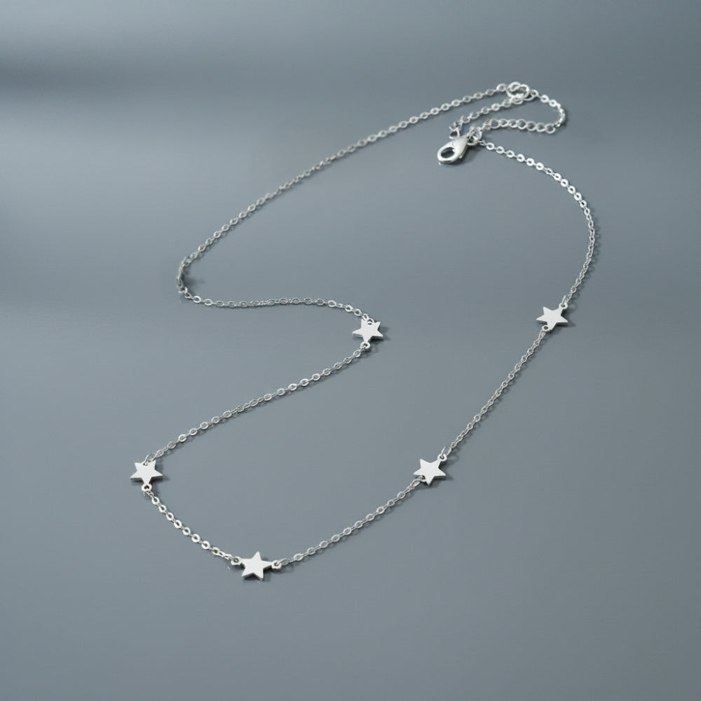 A delicate silver chain necklace featuring five small, evenly spaced star charms, displayed on a smooth, dark gray surface.