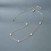 A delicate silver chain necklace featuring five small, evenly spaced star charms, displayed on a smooth, dark gray surface.