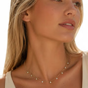 A close-up lifestyle shot of a woman wearing a delicate gold necklace adorned with small star and round bead charms.