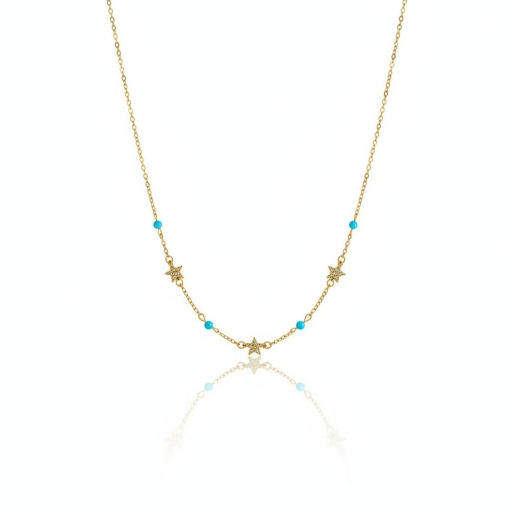 A delicate gold chain necklace featuring small star and crescent moon charms, accented with tiny turquoise blue beads, displayed on a clean white background with a soft reflection.
