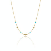A delicate gold chain necklace featuring small star and crescent moon charms, accented with tiny turquoise blue beads, displayed on a clean white background with a soft reflection.