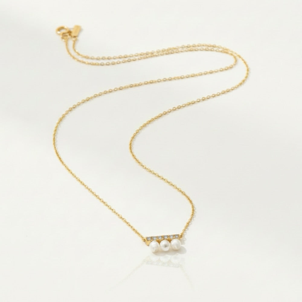 A delicate gold chain necklace featuring a bar pendant with three small white pearls and tiny clear stones, displayed on a clean white background.