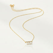 A delicate gold chain necklace featuring a bar pendant with three small white pearls and tiny clear stones, displayed on a clean white background.