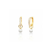 A pair of gold huggie hoop earrings with small clear pavé stones and a dangling white pearl, shown on a clean white background with a soft reflection below.