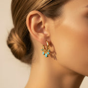 A close-up of a model's ear wearing a gold huggie hoop earring adorned with small turquoise blue beads and delicate gold filigree.