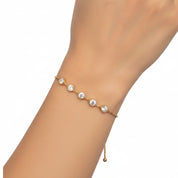 A delicate gold chain bracelet with five clear round-cut gemstones, shown worn on a person's wrist against a plain white background.