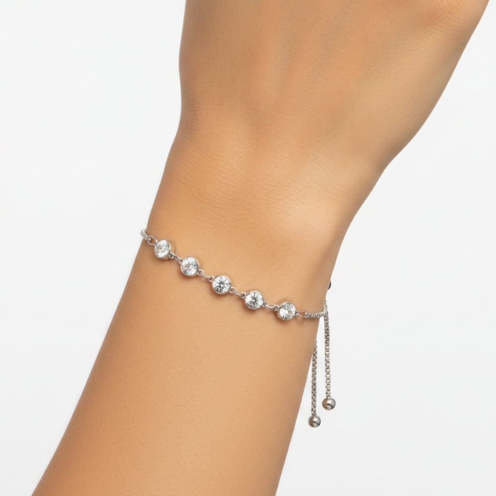 A delicate silver chain bracelet with five clear round-cut stones and two dangling bead chains, shown worn on a person's wrist against a plain white background.