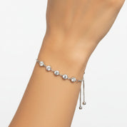 A delicate silver chain bracelet with five clear round-cut stones and two dangling bead chains, shown worn on a person's wrist against a plain white background.