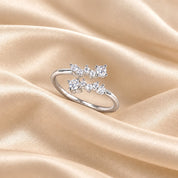 A silver ring with three small clear gemstones arranged in a bow-like cluster, photographed on draped champagne satin fabric.