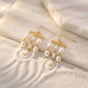 Pair of pearl earrings with gold hooks on a textured beige surface