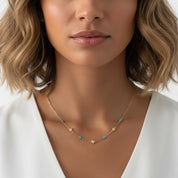 A close-up of a woman wearing a delicate gold necklace with small star and turquoise bead accents, paired with a white top.