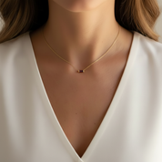 A close-up of a woman wearing a delicate gold chain necklace with a small rectangular dark red stone pendant, paired with a white V-neck top.