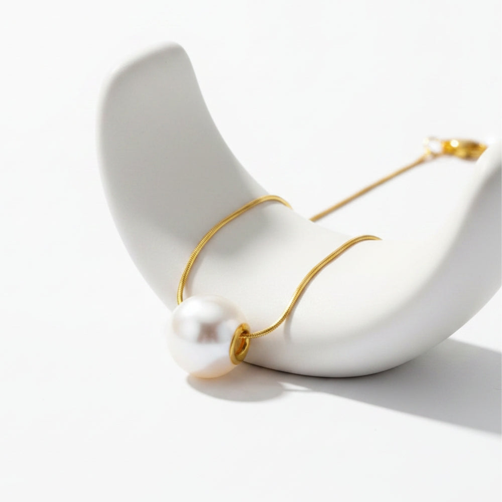A delicate gold necklace with a single white pearl pendant, displayed on a white crescent-shaped jewelry stand against a clean white background.