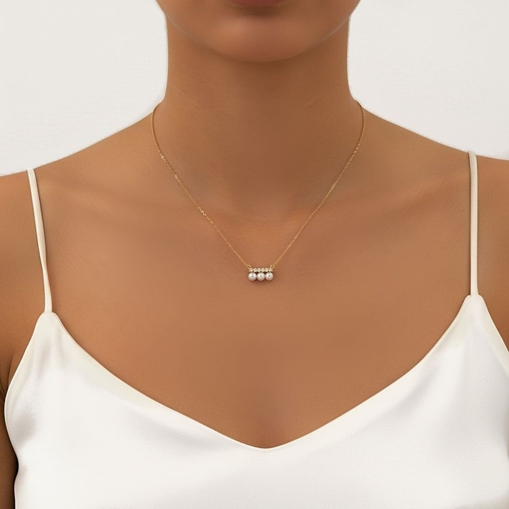 A delicate gold chain necklace with a small cluster of three white pearls at the center, shown worn on a model's neck over a white camisole top.