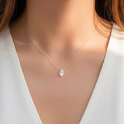 A close-up of a model wearing a delicate silver chain necklace with a marquise-cut clear gemstone pendant, styled with a white V-neck top.