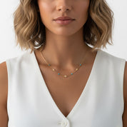 A close-up of a woman wearing a delicate gold necklace with small star and turquoise bead details, paired with a white sleeveless top.