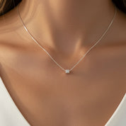 A delicate silver chain necklace with a small, polished square pendant, shown worn on a model's neck.