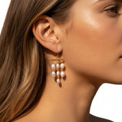 A close-up of a woman's ear wearing a gold dangle earring with three small white pearl drops.