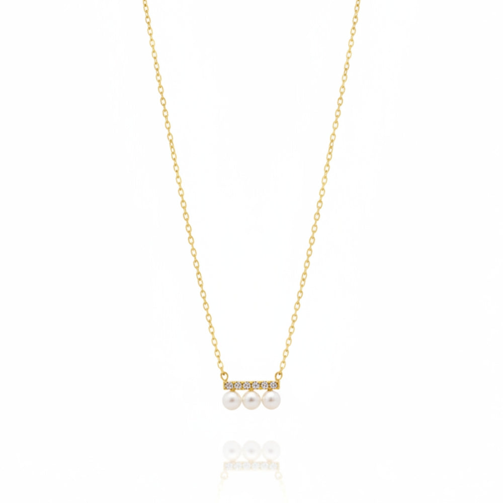 A delicate gold chain necklace featuring a small horizontal bar with three white pearls and tiny clear stones, displayed on a clean white background with a soft reflection below.