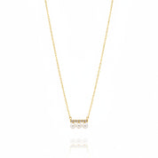 A delicate gold chain necklace featuring a small horizontal bar with three white pearls and tiny clear stones, displayed on a clean white background with a soft reflection below.