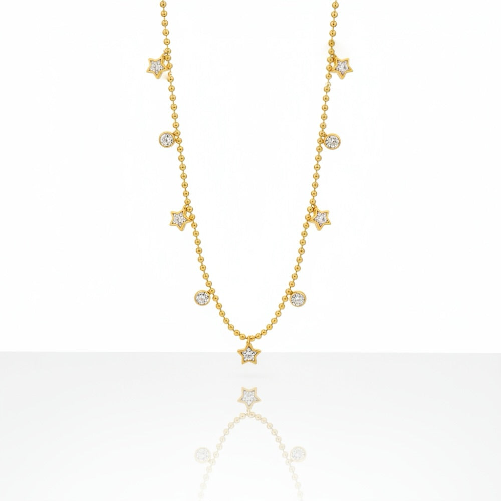A delicate gold necklace featuring small star and round stone charms, displayed against a clean white background with a soft reflection below.
