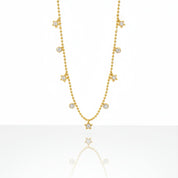 A delicate gold necklace featuring small star and round stone charms, displayed against a clean white background with a soft reflection below.
