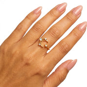 A gold crescent moon ring with small clear gemstones, shown worn on a hand with manicured nails against a white background.