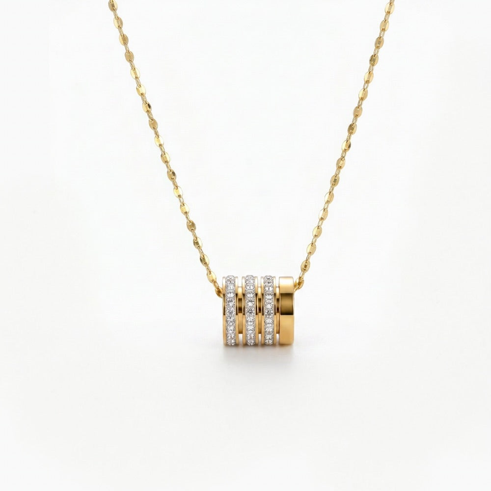 A gold necklace with a cylindrical pendant featuring three vertical bands of small clear stones, shown on a plain white background.