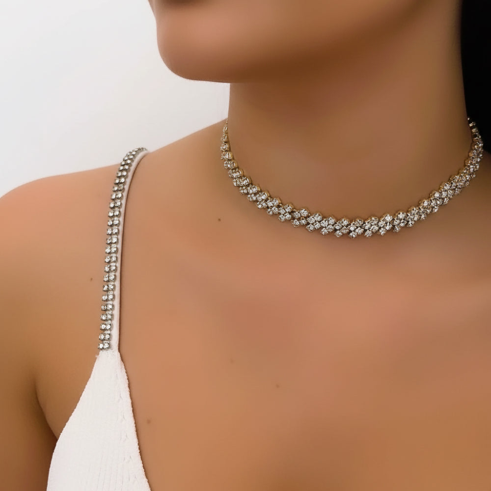 A close-up of a model wearing a gold rhinestone choker necklace and a white spaghetti-strap top against a plain light background.
