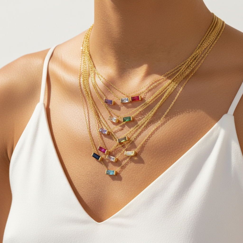 A close-up of a model wearing a layered gold necklace set with multiple small rectangular colorful gemstone pendants, styled with a white sleeveless top.